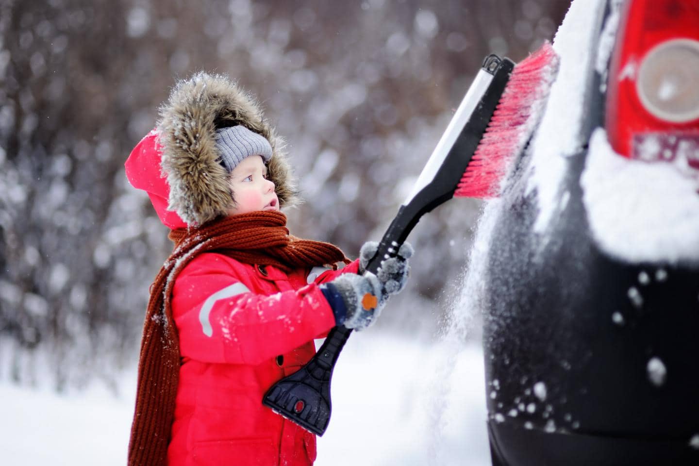 Pige gør bilen klar til vinter, hun børster sne og frost af bilen