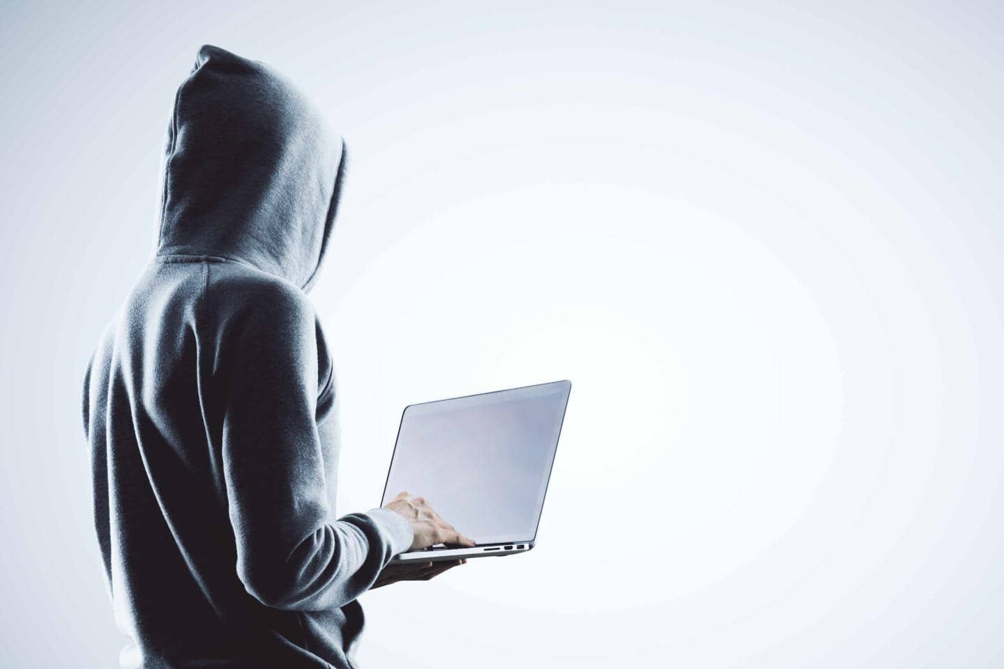 Mand med hætte over hovedet, der står med en bærbarcomputer