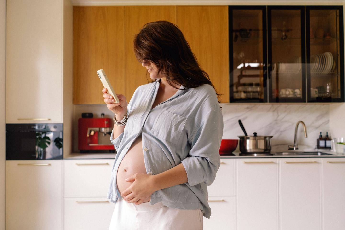 Gravid kvinde i køkken kigger på telefon