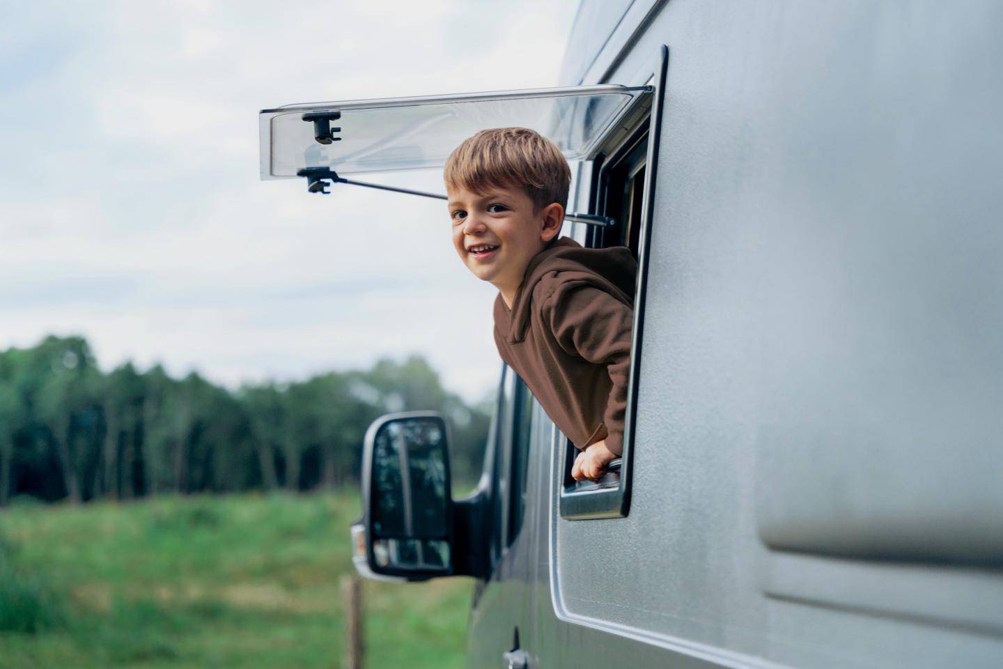 Dreng hænger ud af vindue på autocamper og smiler, fotografi